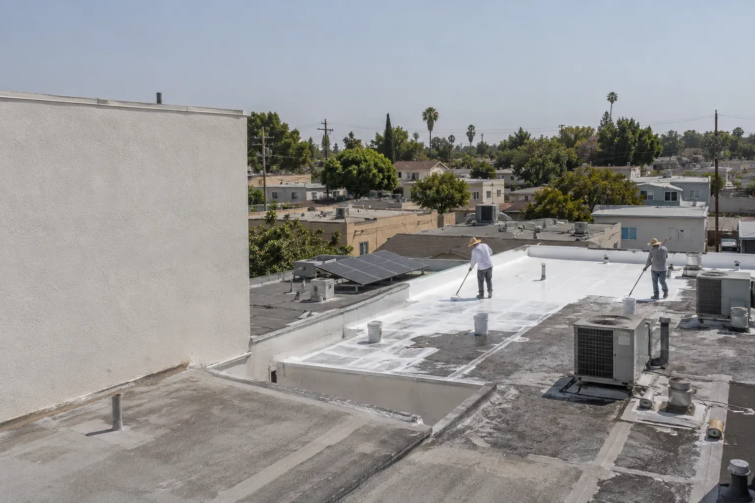 White cool-roof coating going onto a low-slope roof among dark roofs